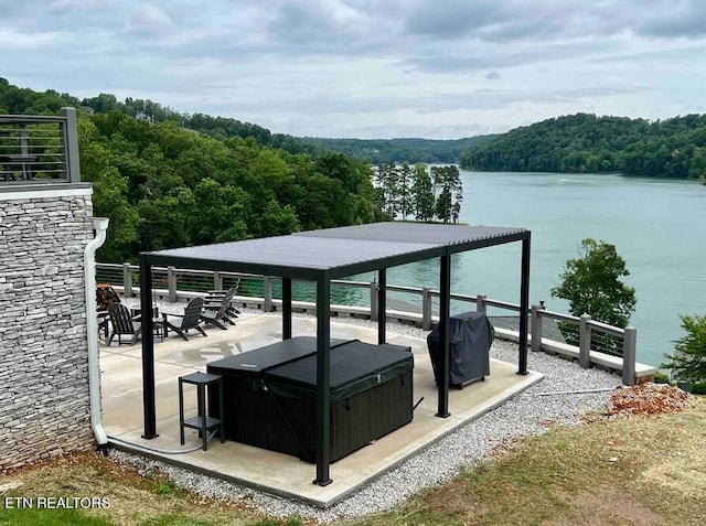 view of patio / terrace featuring a view of trees, a hot tub, a grill, and a water view