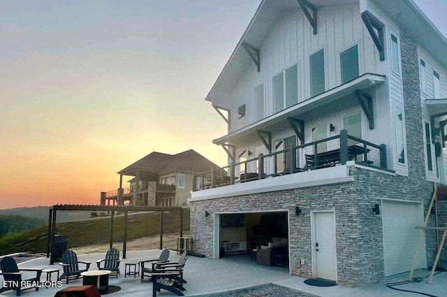 rear view of house with an attached garage, stone siding, a patio, and a balcony