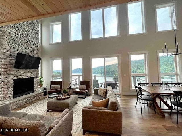 living area with a stone fireplace, a water view, wood ceiling, a towering ceiling, and wood-type flooring
