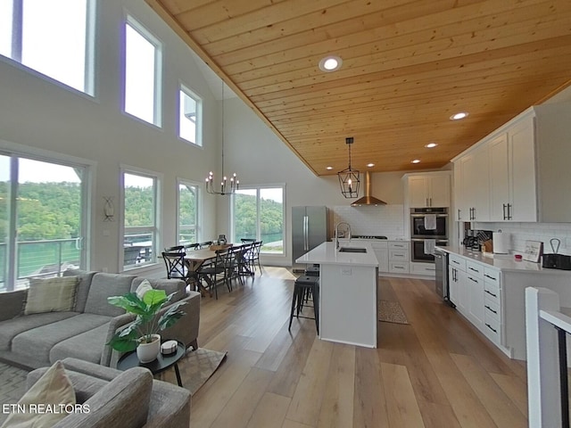 kitchen with a sink, wood ceiling, an inviting chandelier, stainless steel appliances, and wall chimney exhaust hood