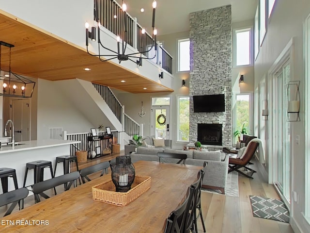 dining room featuring a chandelier, a towering ceiling, light wood finished floors, a fireplace, and visible vents