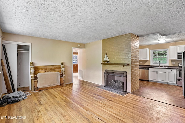 unfurnished living room with a textured ceiling, a sink, light wood-type flooring, a brick fireplace, and visible vents