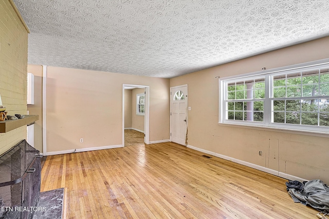 unfurnished living room with a textured ceiling, a fireplace with flush hearth, light wood finished floors, baseboards, and visible vents