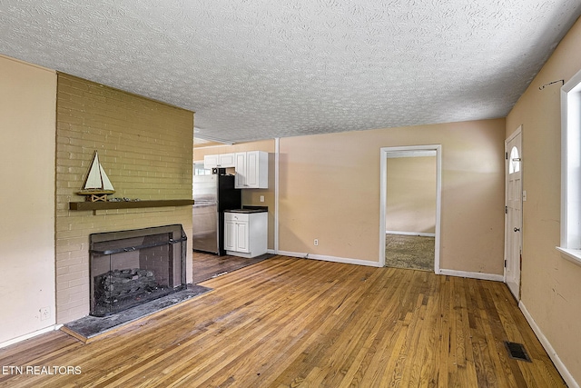unfurnished living room featuring a brick fireplace, hardwood / wood-style floors, visible vents, and a textured ceiling