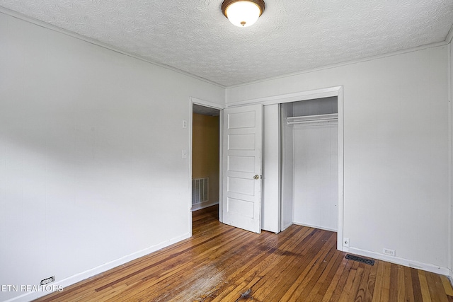 unfurnished bedroom featuring a textured ceiling, a closet, wood-type flooring, baseboards, and visible vents