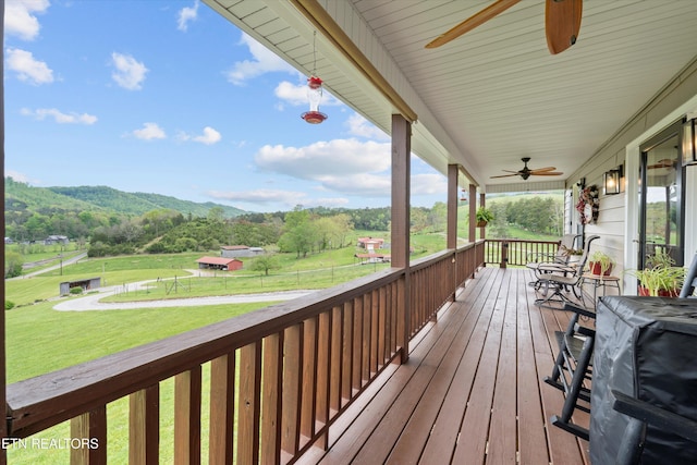 wooden deck with ceiling fan, covered porch, a yard, and a mountain view