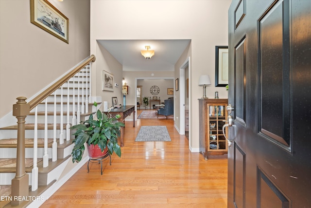 entryway with light wood-style floors, stairway, a towering ceiling, and baseboards