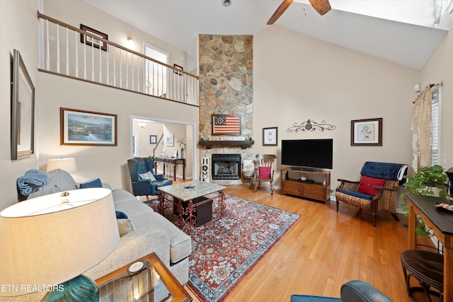 living room with wood finished floors, a stone fireplace, high vaulted ceiling, and ceiling fan