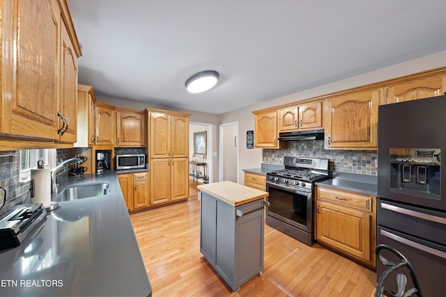 kitchen featuring light wood-style flooring, a sink, backsplash, under cabinet range hood, and appliances with stainless steel finishes