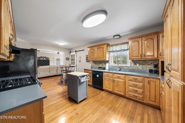 kitchen featuring light wood-style flooring, a sink, a barn door, decorative backsplash, and black appliances