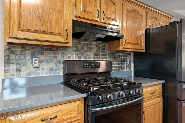 kitchen featuring under cabinet range hood, light countertops, stainless steel range with gas stovetop, freestanding refrigerator, and decorative backsplash