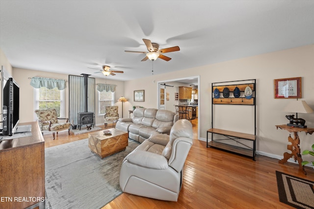 living area with baseboards, a ceiling fan, wood finished floors, and a wood stove