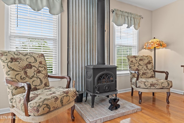 sitting room with plenty of natural light, baseboards, wood finished floors, and a wood stove
