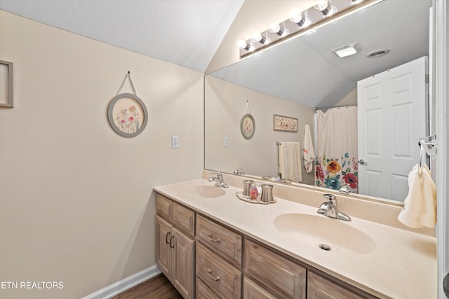 bathroom with double vanity, lofted ceiling, baseboards, and a sink