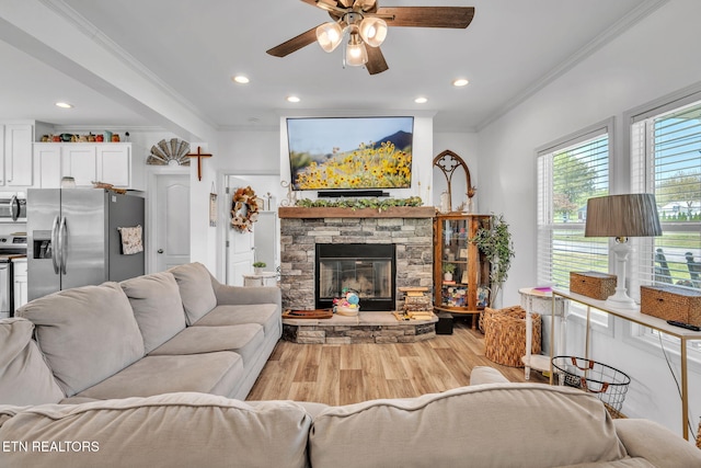 living area featuring a ceiling fan, a stone fireplace, light wood-style floors, ornamental molding, and recessed lighting