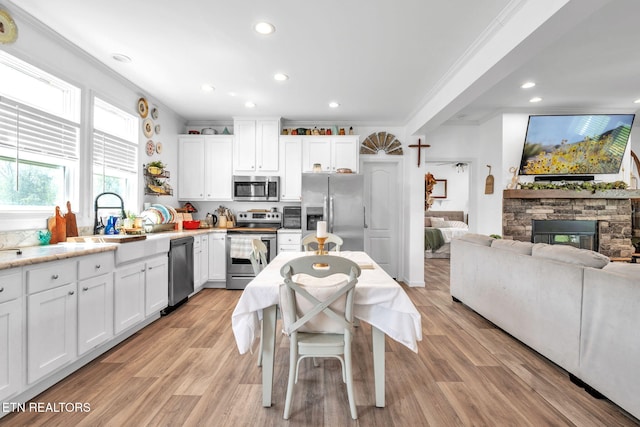 kitchen featuring a sink, open floor plan, white cabinetry, crown molding, and appliances with stainless steel finishes