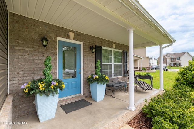 property entrance featuring a yard, a porch, and brick siding