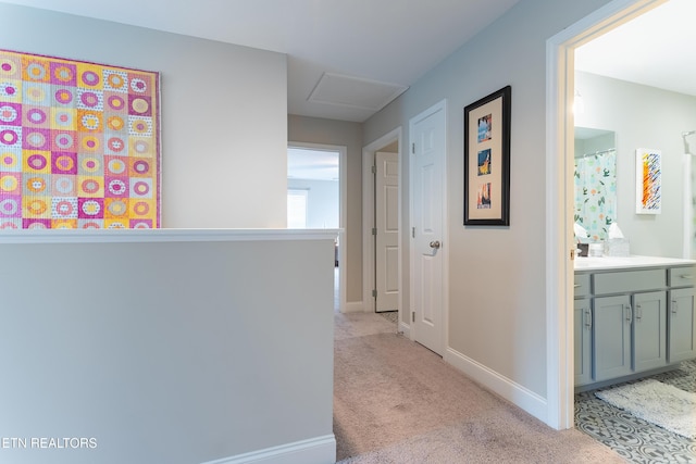 hallway featuring light colored carpet, attic access, and baseboards