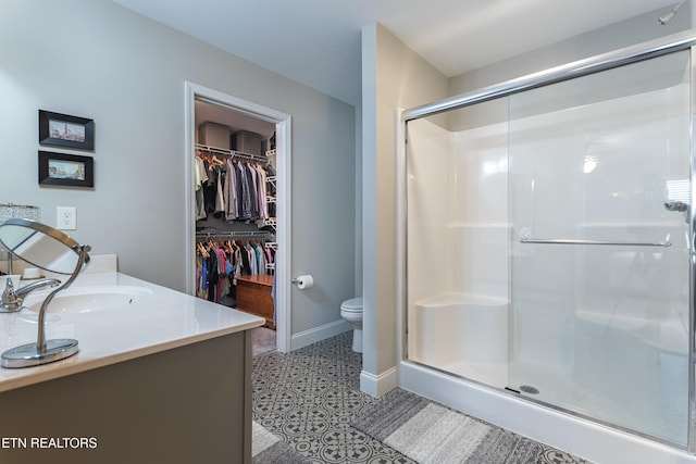 bathroom with a shower stall, toilet, a walk in closet, vanity, and baseboards