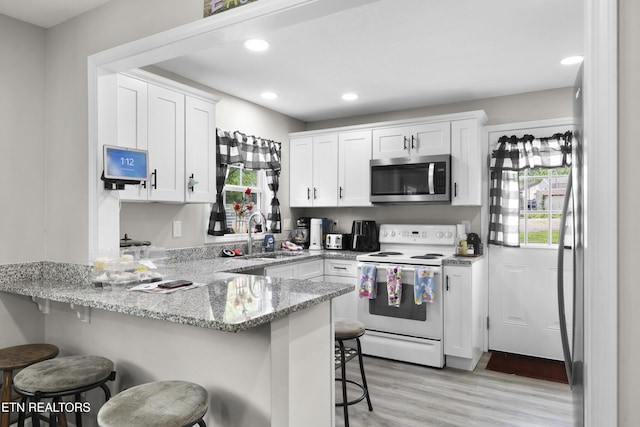 kitchen with stainless steel microwave, a sink, white range with electric stovetop, a peninsula, and white cabinets
