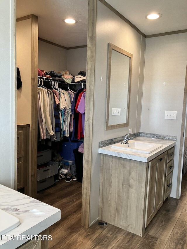 full bath featuring wood finished floors, a spacious closet, vanity, and crown molding