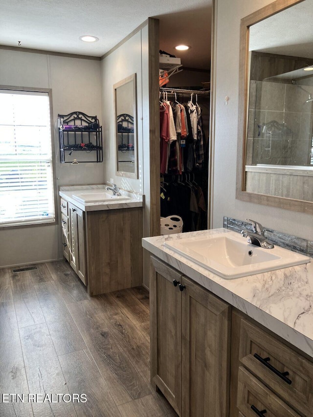 full bathroom with wood finished floors, a walk in closet, vanity, a tile shower, and visible vents
