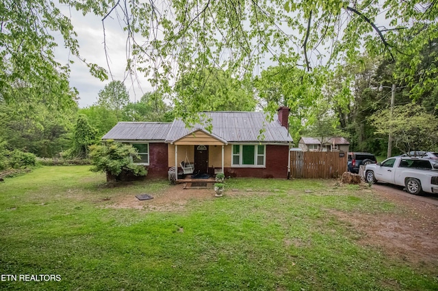 view of front of house featuring a chimney, a front lawn, fence, metal roof, and brick siding