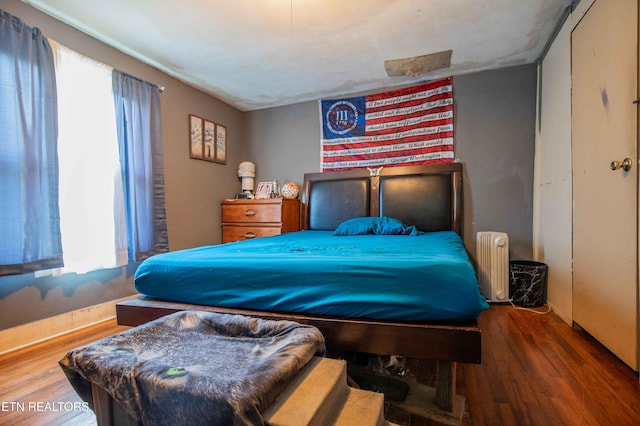 bedroom featuring radiator heating unit, wood finished floors, baseboards, and multiple windows