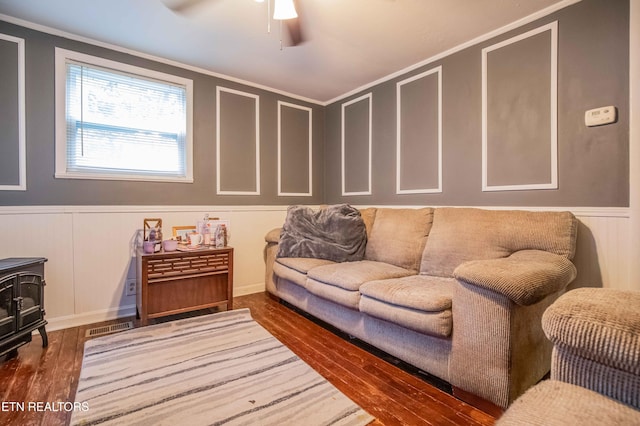 living room with visible vents, wood finished floors, a wood stove, and a decorative wall