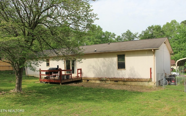 back of property featuring a deck, fence, a shingled roof, and a lawn