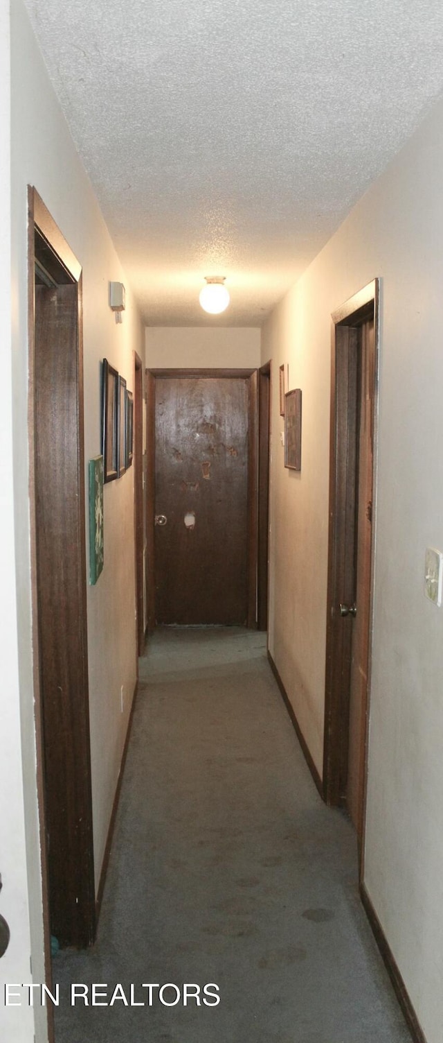 corridor featuring a textured ceiling, carpet, and baseboards