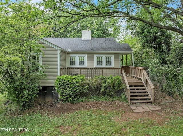 rear view of house with a chimney, a deck, and a shingled roof