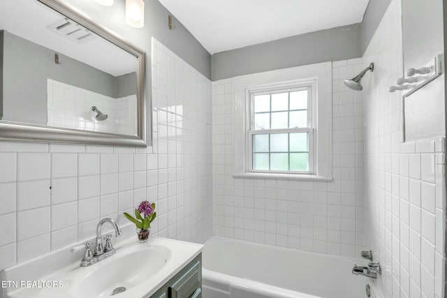 bathroom with tile walls, washtub / shower combination, vanity, and visible vents