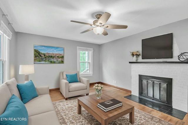 living room featuring wood finished floors, baseboards, a ceiling fan, and a brick fireplace