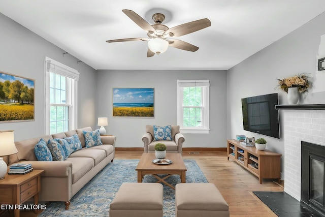 living room with a fireplace, light wood finished floors, baseboards, and a ceiling fan