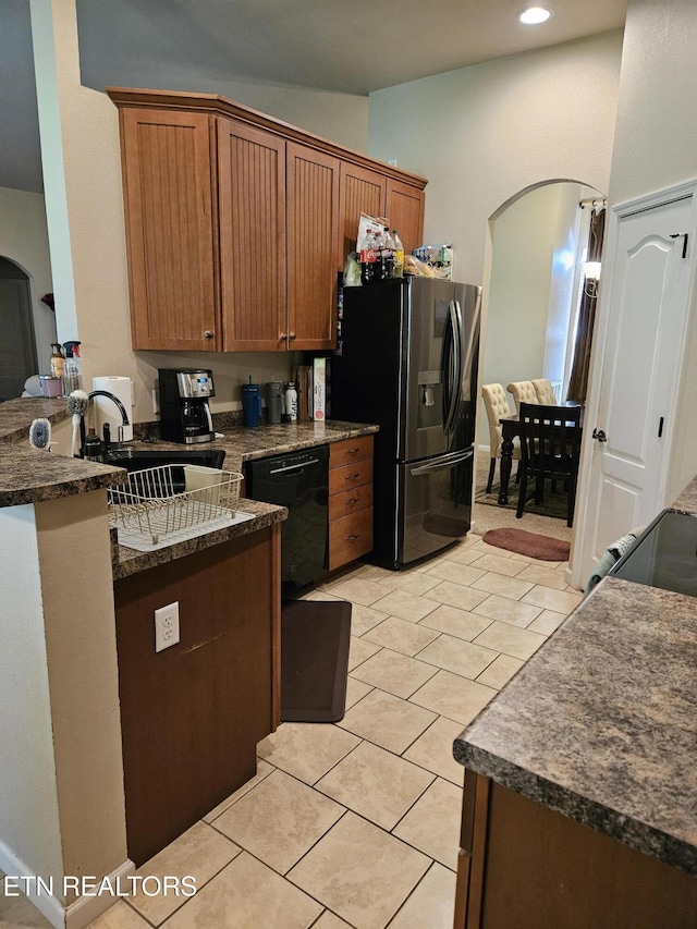 kitchen featuring dark countertops, brown cabinetry, black appliances, light tile patterned floors, and arched walkways