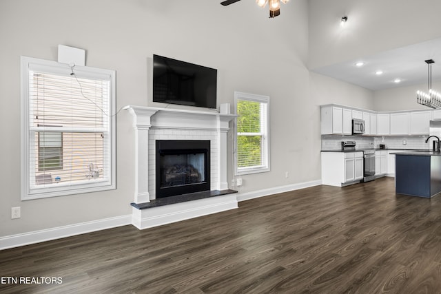 unfurnished living room with ceiling fan, a fireplace, a sink, baseboards, and dark wood-type flooring