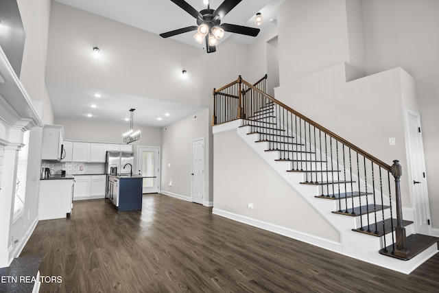 unfurnished living room featuring a high ceiling, dark wood finished floors, and ceiling fan