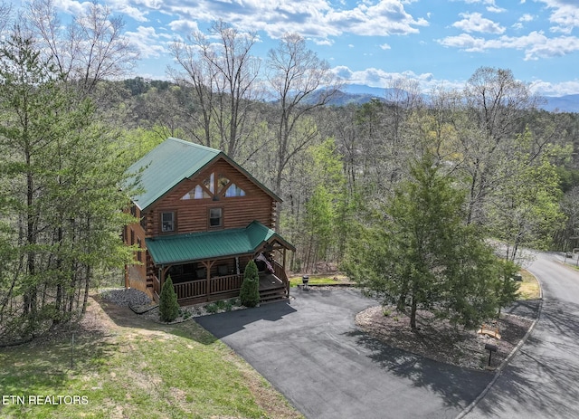 view of front facade featuring log exterior, driveway, a porch, a view of trees, and metal roof