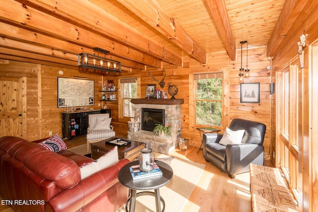 living area with beamed ceiling, wooden walls, a stone fireplace, wood ceiling, and wood finished floors