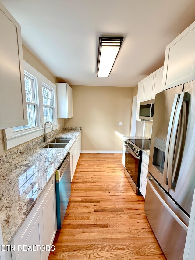 kitchen with white cabinets, stainless steel appliances, a sink, light wood-type flooring, and light stone countertops