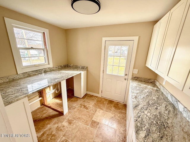 doorway to outside featuring plenty of natural light, baseboards, stone tile flooring, and built in desk