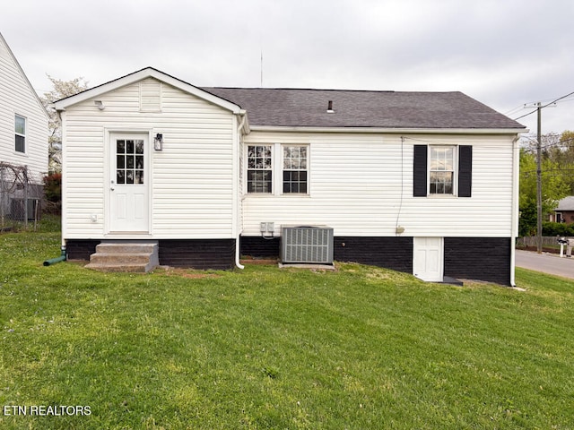 rear view of property with central air condition unit, roof with shingles, a yard, and entry steps