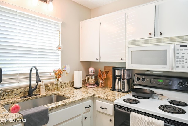 kitchen with electric stove, a sink, white microwave, light stone counters, and white cabinets
