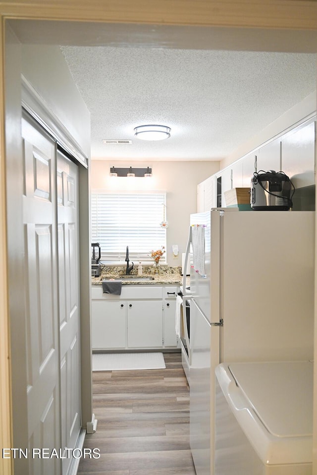 interior space with freestanding refrigerator, a sink, white cabinetry, light wood-type flooring, and a textured ceiling