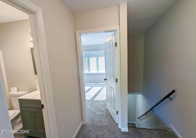 hall featuring an upstairs landing, baseboards, and carpet floors