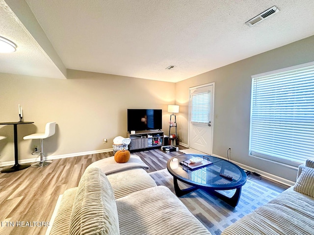 living area featuring baseboards, visible vents, wood finished floors, and a textured ceiling