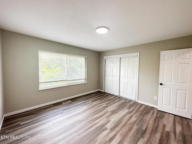 unfurnished bedroom with baseboards, wood finished floors, a textured ceiling, and a closet