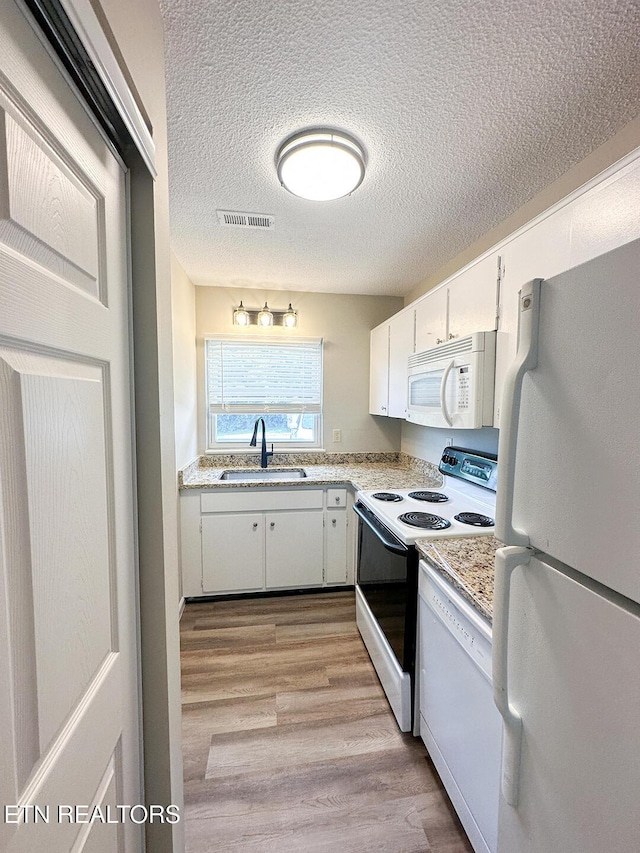 kitchen with white appliances, a sink, white cabinetry, visible vents, and a textured ceiling