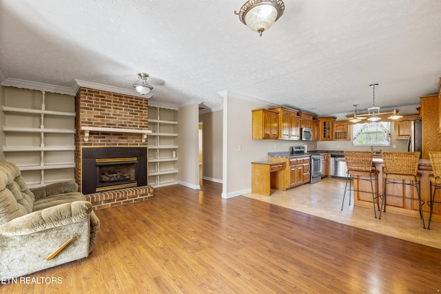 unfurnished living room with light wood-type flooring, a brick fireplace, a textured ceiling, and crown molding